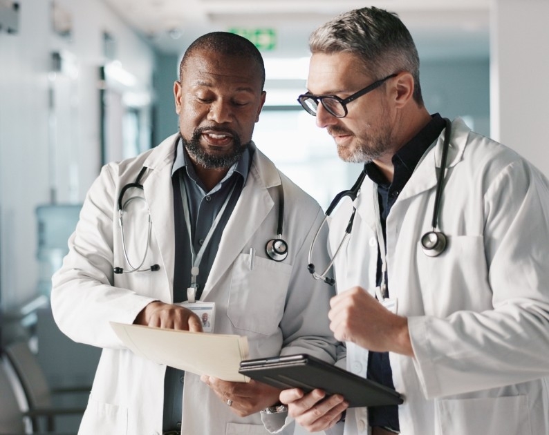 Two physicians reviewing digital patient records in a clinical setting, illustrating managed care performance analysis and outcome-focused healthcare management.